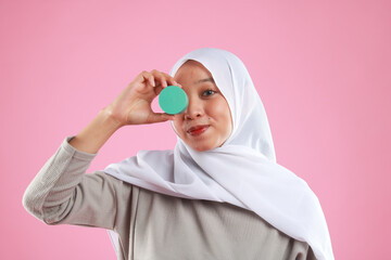 Asian young woman showing skincare products on pink background.