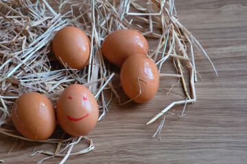 Eggs in a straw and one was written in a smiley face. All laid on a wooden table.