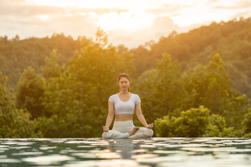 Calm of Beautiful Attractive Asian woman practice yoga Lotus pose on the pool above the Mountain peak in the morning in front of beautiful nature views,Feel so comfortable and relax in holiday