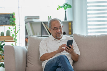 Happiness elderly asian man sitting on sofa using mobile phone and social media smile at home,Senior lifestyle at home concept