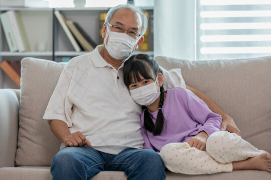 Asian Elderly grandfather hug grandchild and wearing face mask on sofa at home protect virus infection