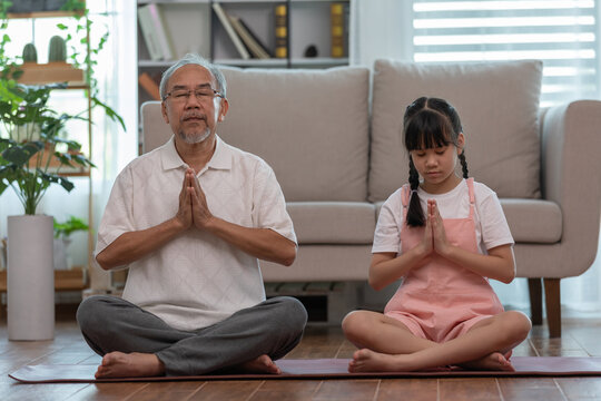 Elderly grandfather and children doing yoga for meditation together in living room at home so happy and comfortable