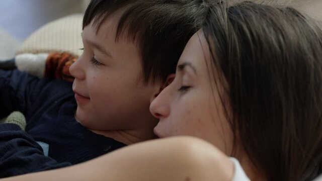 Mother tries to convince toddler boy to nap in arms on couch - close up on faces