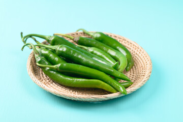 Fresh green chili peppers in a basket on green color background