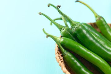 Fresh green chili peppers in a basket on green color background