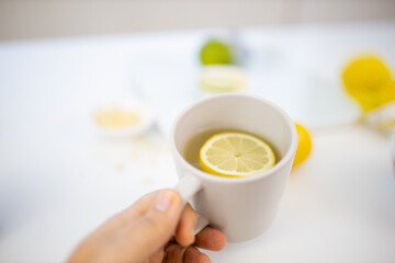 Female hand holding a cup of lemon tea above limes and lemons