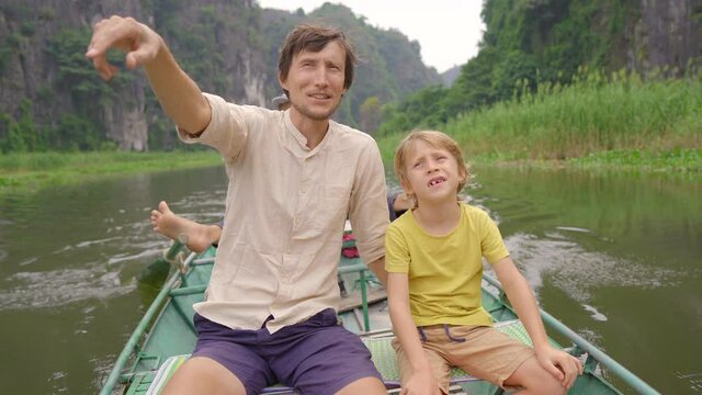 A young man and his son on a boat having a river trip among spectacular limestone rocks in Ninh Binh, a tourist destination in northern Vietnam. Travel to Vietnam concept