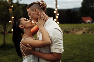 Fototapeta premium Portrait of beautiful elegant couple kissing. Handsome man hugging attractive woman, enjoy tenderness. Gorgeous lady with attractive male walking at the park, spend weekends outdoor together
