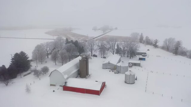 Establishing shot of Midwestern countryside in winter season.  Aerial view of farm, agricultural fields. Cold misty weather with snow and frost
