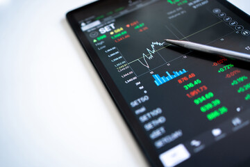 Pen points to the stock market trader's selling price, displayed as a graph on a tablet screen.