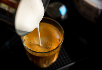 Close focus on pouring steam milk into shot of hot espresso coffee on glass cup.