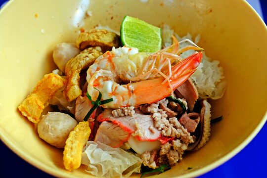 Thai spicy dried rice noodles with assorted seafood, fish balls and deep fried pork crackling in yellow bowl.