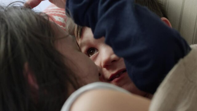 Young boy and mother cuddle up on couch for afternoon nap - close up on faces
