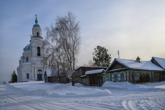 church in the snow. rural street with wooden houses leading to a high church made of white stone (Shurala, Nevyanskiy district, Russia). a lot of snow fell. blue sky with white clouds