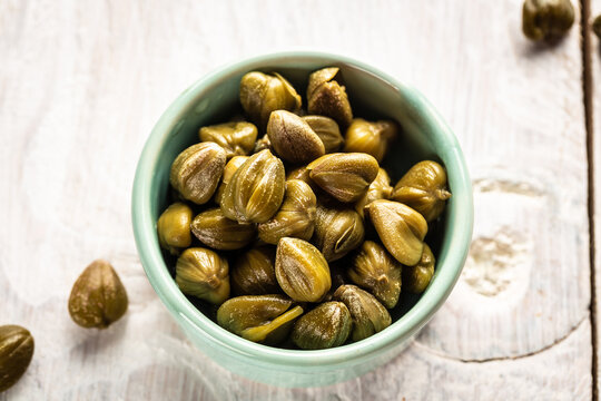 Marinated capers in a ceramic bowl. Edible flower buds of Capparis spinosa, caper bush or Flinders rose on a light background
