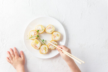 Sushi rolls in the form of a heart on a white plate with the hands of a child. Horizontal orientation, top view.