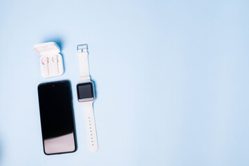 The layout of the watch and the phone on a blue background. Appliances and electronics. Modern gadgets. Phone headphones watch. Business. Wireless headphone. Watch with pedometer.