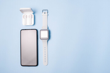 The layout of the watch and the phone on a blue background. Appliances and electronics. Modern gadgets. Phone headphones watch. Business. Wireless headphone. Watch with pedometer.