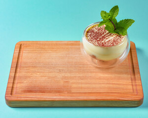 Tiramisu dessert served in a small glass on a wooden board over blue background. Traditional Italian dessert.