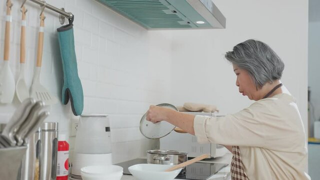 Asian senior woman cooking food and let her husband smelling the soup.