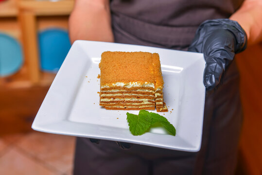 Cake Napoleon served on a white plate. Waiter serving dessert at restaurant or diner, eating out concept.