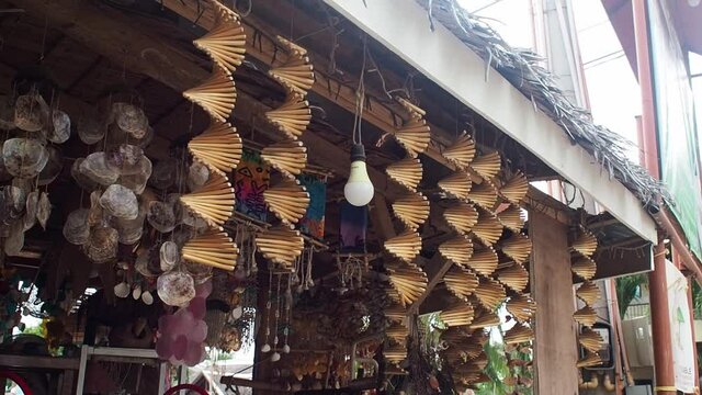 Decorative wooden helix kinetic wind spinners hanging at the front of a tropical souvenir shop. Medium shot.
