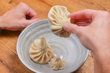Man eats khinkali - Georgian dumpling served in a white bowl over rustic wooden table. Eating, still life.