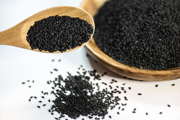 Black sesame on a wooden container, a focus photo overlaying a stick pouring black sesame onto the white background