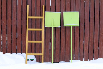 Two green wooden shovels and a yellow ladder stand against the wall of the shed. 