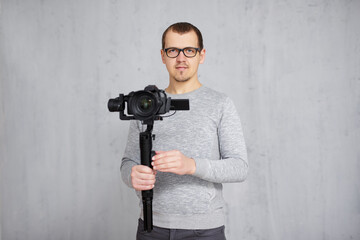 professional videographer holding dslr camera on 3-axis gimbal over grey concrete wall