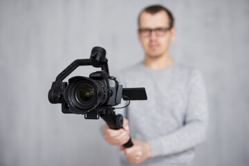 close up of modern dslr camera on 3-axis gimbal stabilizer in videographer hands over grey