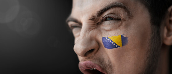 A screaming man with the image of the Bosnia and Herzegovina national flag on his face