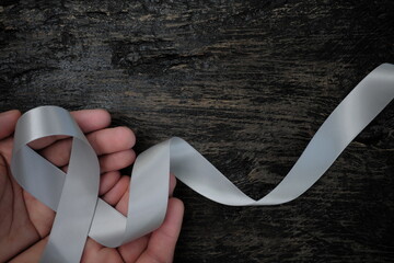 Top view of male hand holding gray ribbon on dark wood background with copy space. Brain cancer tumor awareness concept.