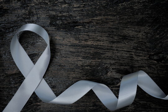 Top view of gray ribbon on dark wood background with copy space. Brain cancer tumor awareness concept.