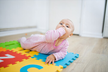 Adorable baby lying on a colorful mat with her fist in her mouth