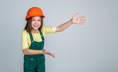 girl kid in hard hat on construction site, presenting product, copy space for advertisement