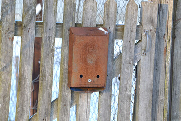 Old rusty metal mailbox on a wooden fence