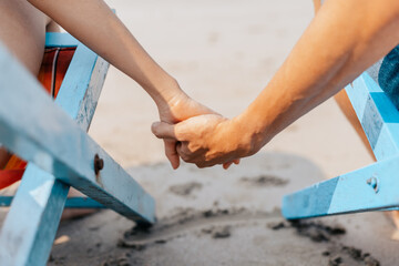 Couple of lovers sitting on beach chair holding hands on the beach in the morning.  Newlywed couple on a romantic vacation