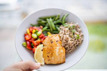 Hand holding salmon and buckwheat dish with green beans