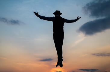 silhouette of man float in sunrise sky with raised hands, freedom