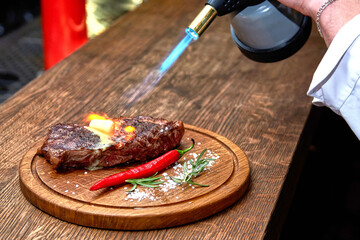 Master chef cooking barbecue Beef Grilled steak meat with fire flames on wooden table