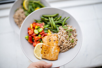 Hand holding salmon and buckwheat dish with green beans
