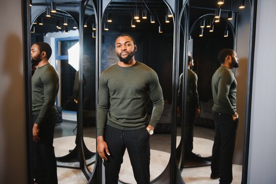 Stylish casual african american man at fitting room clothes store, looking on mirror. The concept of stylish men's clothing.