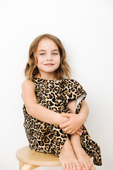 Portrait of a girl, she sits and hugging her knees in a leopard print dress. High quality photo