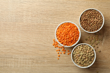 Bowls with different legumes on wooden background, space for text