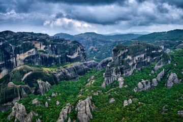 Fototapeta na wymiar View over impressive pillars of sedimentary rocks in iconic Meteora valley at cloudy spring day. Hills covered with trees, winding roads, Greece