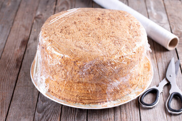 Honey cake packed in cling film on a wooden table. Frozen cake