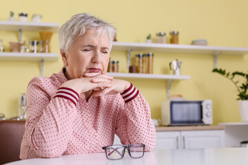 Stressed senior woman suffering from headache at home