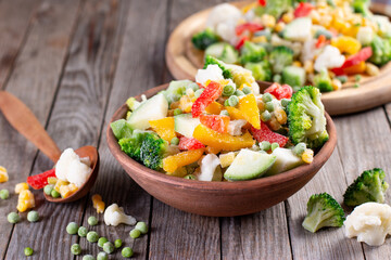Frozen vegetables: a mix of vegetables in a bowl on wooden table. Close-up with a copy space. Horizontal orientation.