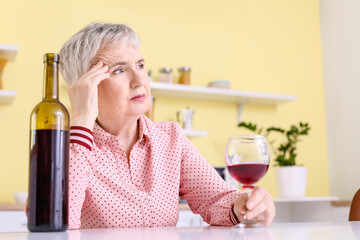Stressed senior woman drinking wine at home
